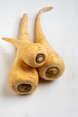 Top view of three parsnips on white wooden table, vertical with copy space