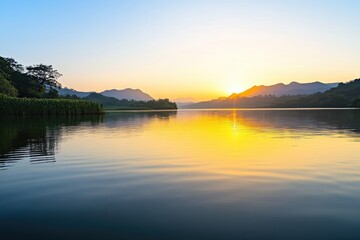 Fototapeta premium serene lakeside scene at sunrise with calm water reflecting golden hues of sky surrounded by greenery and distant mountains
