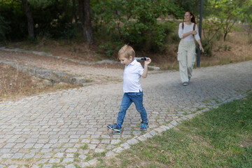 Obraz premium Little boy playing with binoculars walking in park with mother
