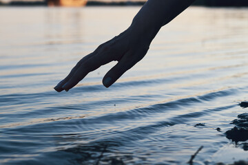 hand gently reaches towards the rippling water, creating a serene and reflective moment.