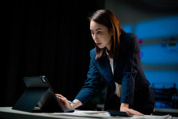 Businesswoman concentrating on her work on a tablet with stylus pen, working late in a dimly lit...