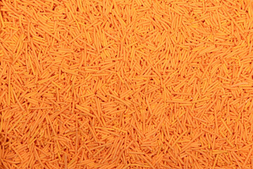 Close-up of uncooked orange vermicelli pasta, small cylindrical noodles scattered in a textured background. Detailed food texture ideal for culinary, packaging, and ingredient concepts.