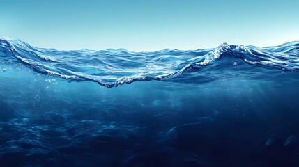Deep blue ocean waves with underwater view showing crystal clear waters and dynamic surface movement against bright sky, suitable for environmental themes.