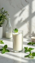 Glass of milk with a mint leaf garnish on a marble countertop.