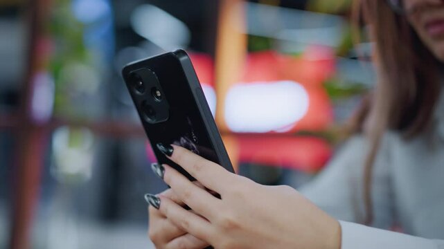 Close-up of black painted nails holding iPhone with donkey sticker as owner operates it with blurred background, focus on personalized phone case and stylish nails in casual setting