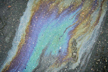 An oil slick spreads across asphalt, displaying vibrant colors including blue and purple. The...