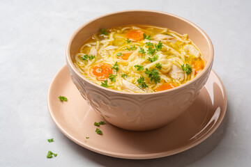 Chicken soup with noodles and vegetables in bowl on concrete background