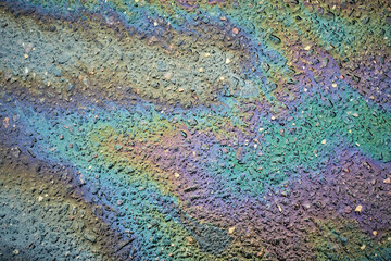 Vibrant swirls of color from an oil slick form intricate patterns on a wet pavement in an urban...