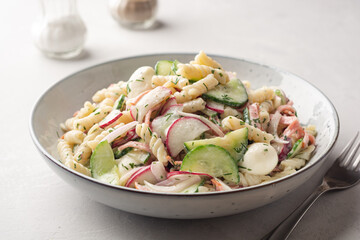 Pasta salad with vegetables, sausage and mozzarella cheese in plate on concrete background