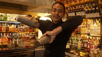 Smiling Asian smart bartender shaking with two hands in mixed cocktail in shaker preparing at...