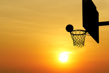 Basketball Hoop Silhouetted Against a Vibrant Sunset Sky with Glowing Sun in the Background