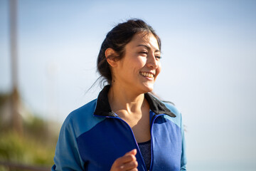 Happy woman jogging in a blue sports jacket on a bright sunny day, enjoying outdoor fitness.