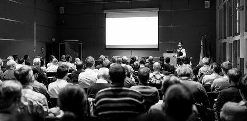 Speaker giving a talk in conference hall at business meeting event. Rear view of unrecognizable people in audience at the conference hall. Business and entrepreneurship concept.