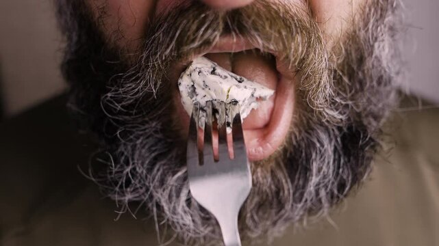 Close up of bearded man eating dorblu cheese taking piece off fork