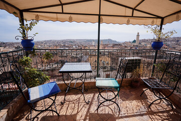 A rooftop terrace with wrought iron furniture and potted plants, overlooking a cityscape with a...
