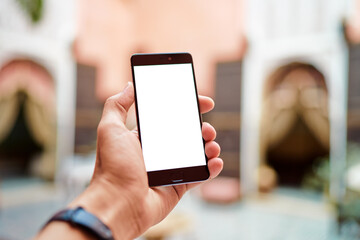A person holding a smartphone with a blank screen in an outdoor setting.