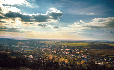 Breathtaking panoramic view of a rural village with rolling hills, lush fields, and a dramatic sky. Idyllic countryside, golden hour, nature, and peaceful landscape.