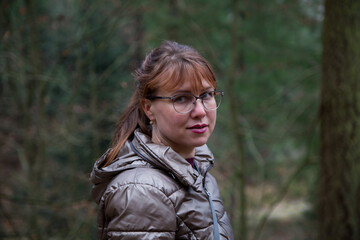 Contemplation in the Woods. A woman in a metallic puffer jacket stands in a forest, gazing off to...