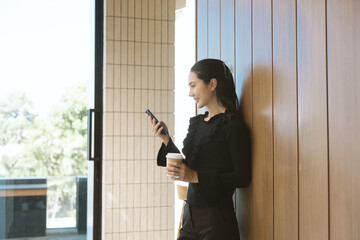 Modern Moment: A smiling professional woman leaning casually against a wooden wall, engrossed in...