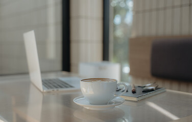 Morning Productivity: A focused scene features a laptop and coffee cup set on a bright table, a scene of work in progress, capturing the ambiance and the elements of a productive workday.