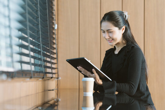 Focused Professional: An elegant woman in a professional setting, engrossed in her tablet, embodies modern productivity and effortless focus, underscored by natural light and a touch of caffeine.