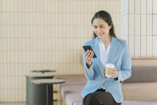 Businesswoman on break: An Asian businesswoman takes a moment of relaxation, sitting gracefully with a warm beverage and a smartphone, exuding modern professionalism.