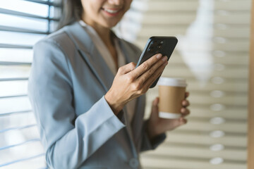 Modern Business Communication: A businesswoman stays connected with her phone while holding a cup of coffee. The photo showcases business professionalism, the fast-paced communication world.
