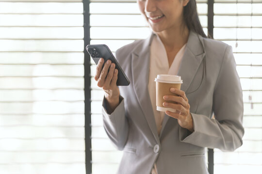 A Modern Pause: A smiling professional woman in a smart suit takes a moment with her phone and a coffee