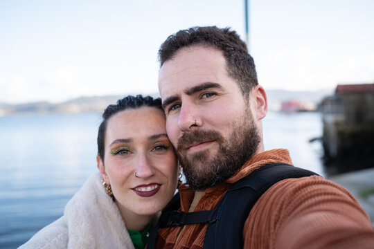 Young tourists capturing selfie amid traditional horreos, exploring picturesque coastal scenery in combarro, galicia, savoring romantic vacation moments by seaside