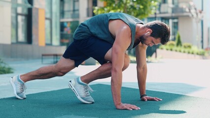 Young man exercising outside. Video process of guy doing mountain climber exercise. Running fast in horizontal position on the same place. Training near urban view.