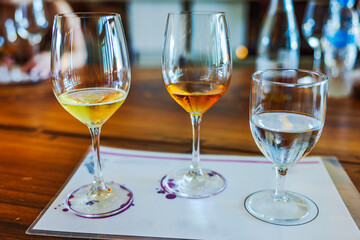Close-up view of three wine glasses filled with white wine, amber wine and water on wooden table. Mexico. 