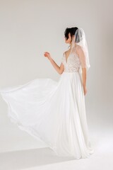Elegant bride twirling in a flowing wedding dress with a veil against a soft, neutral background