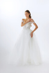 Fototapeta premium Elegant bride in a stunning white gown posing gracefully against a minimalistic backdrop in bright light