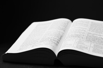 Open Holy Bible in English language on black table, closeup