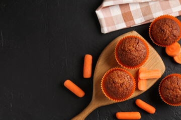 Delicious carrot muffins with fresh vegetables on black table, flat lay. Space for text