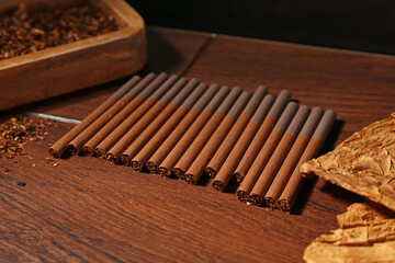 Dried tobacco leaves and cigarettes on wooden table, closeup
