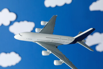 Plane model flying among paper clouds against blue background, closeup