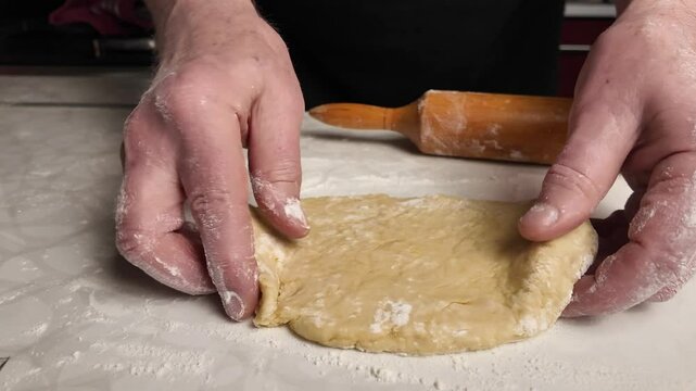 Person rolling out dough on a table in a kitchen, making a shortbread pie     