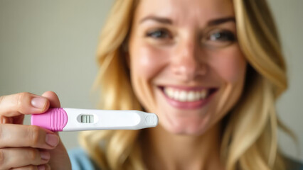 Smiling blonde woman holding out a positive pregnancy test. Concept of: Excitement of pregnancy announcement.
