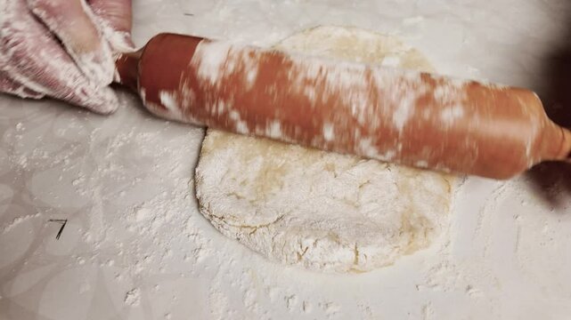 Person rolling out dough on a table in a kitchen, making a shortbread pie