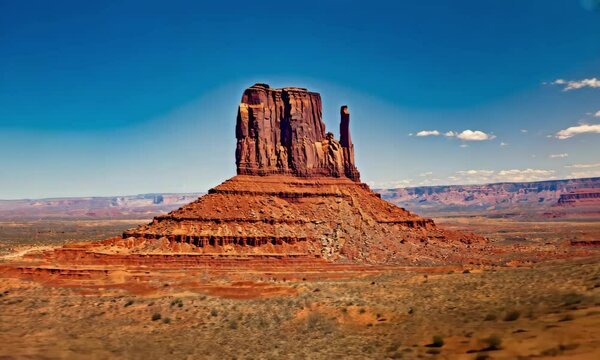 Majestic sandstone butte towering over the desert landscape under a clear blue sky, with distant mesas
