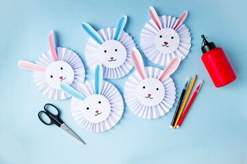 Paper craft on a blue background cute, funny Easter bunnies made of paper, glue, scissors, felt-tip pens.  Concept holiday Easter, spring children's creativity, handmade.  Flat lay, top view.