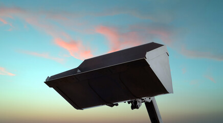 Excavator loader bucket silhouetted against a colorful dawn sky with soft pastel clouds