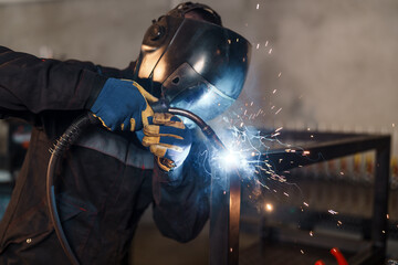 Naklejka premium Professional welder in protective gear joining metal profiles with migmag welding, generating bright sparks and smoke in an industrial workshop