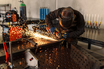 Metalworker wearing safety equipment uses an angle grinder, producing a shower of sparks while working on a metal component in a workshop