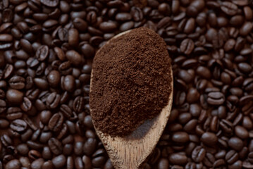 Roasted coffee beans and coffee powder on a wooden table. Wooden spoon with ground coffee inside.
