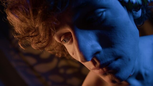 Extreme close-up portrait of frightened Caucasian curly-haired young man with flower behind his ear looking around feeling flustered