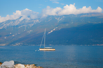 summer scenery, blue lake Gardasee with sailboat, Monte Baldo mountain, italy