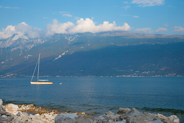 summer scenery, blue lake Gardasee with sailboat, Monte Baldo mountain, italy