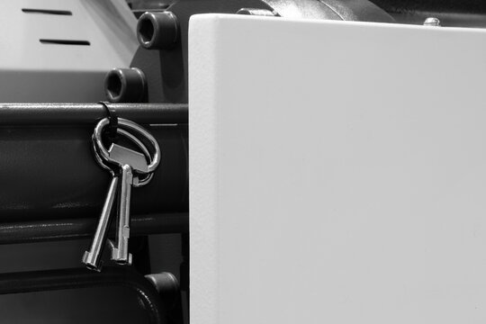 A key is hanging from a metal bar. The key is silver and has a black handle. Concept of security and protection, as the key is used to lock and unlock doors - Powered by Adobe